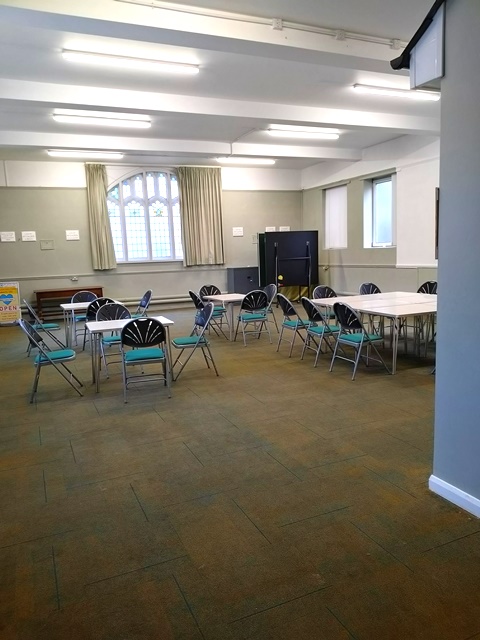 Green chairs and tables set up in the hall with stained glass windows at the end of the room.