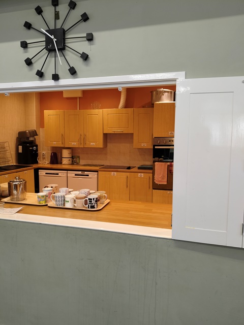 View into the kitchen through the hatch in the hall. Heritage green wall colour in the hall with white hatch doors, showing an orange colour kitchen.
