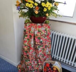 Harvest decorations in the entrance to the church from a previous Harvest service, including a brightly coloured flower display and a basket of fresh vegetable produce.